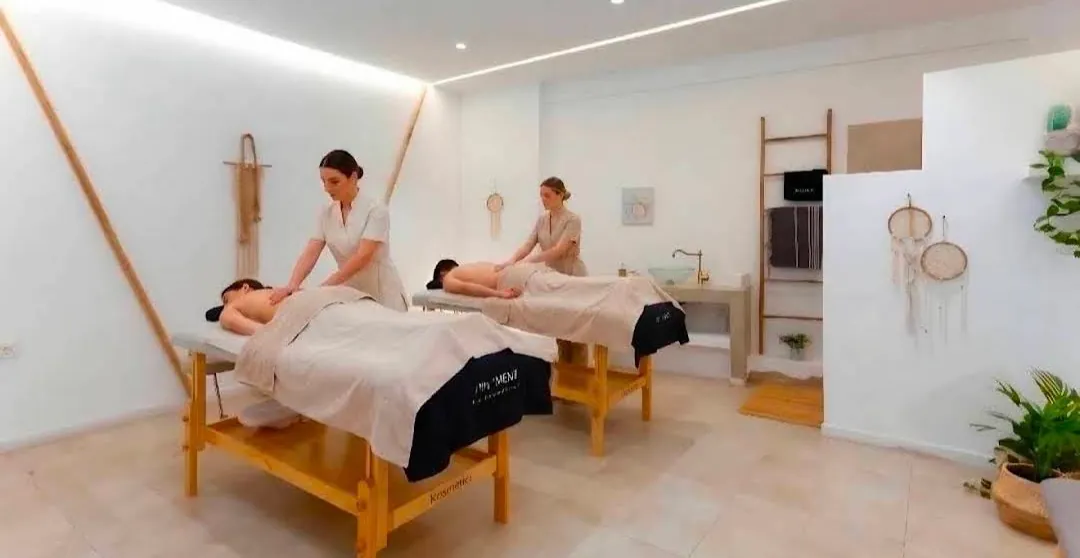 Two massage professionals giving side-by-side back massages in a bright couples room