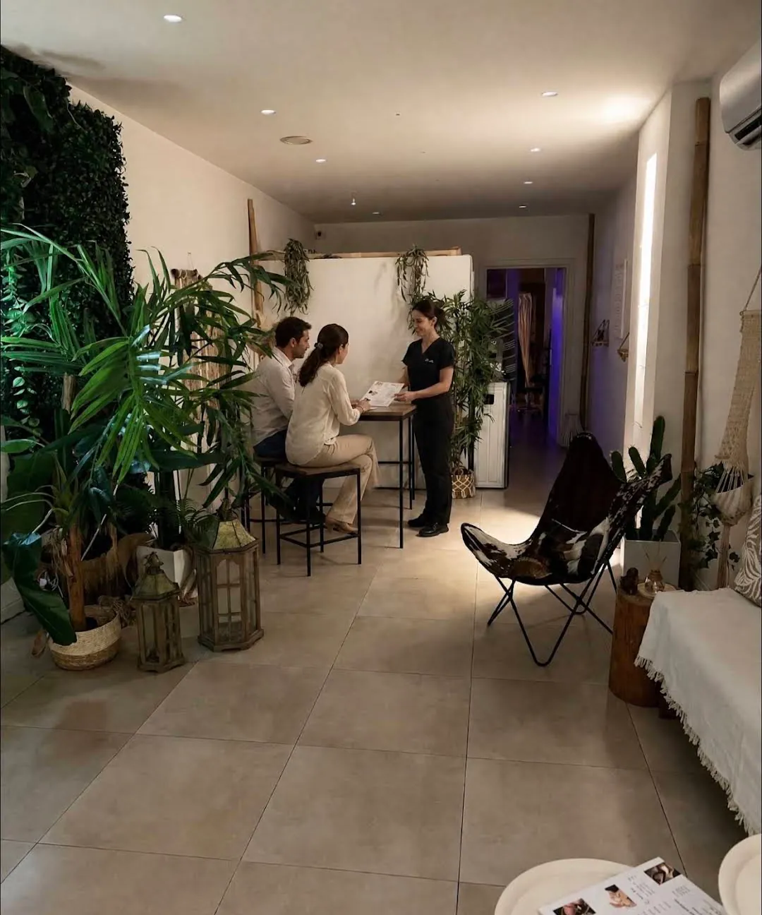 A massage professional presenting the treatment menu to two guests in the plant-filled reception